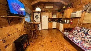 L’intérieur chaleureux d’un chalet avec des murs en bois, une télévision, un lave-linge, un réfrigérateur, un four à micro-ondes, une cuisinière, un évier et un lit recouvert d’une courtepointe.