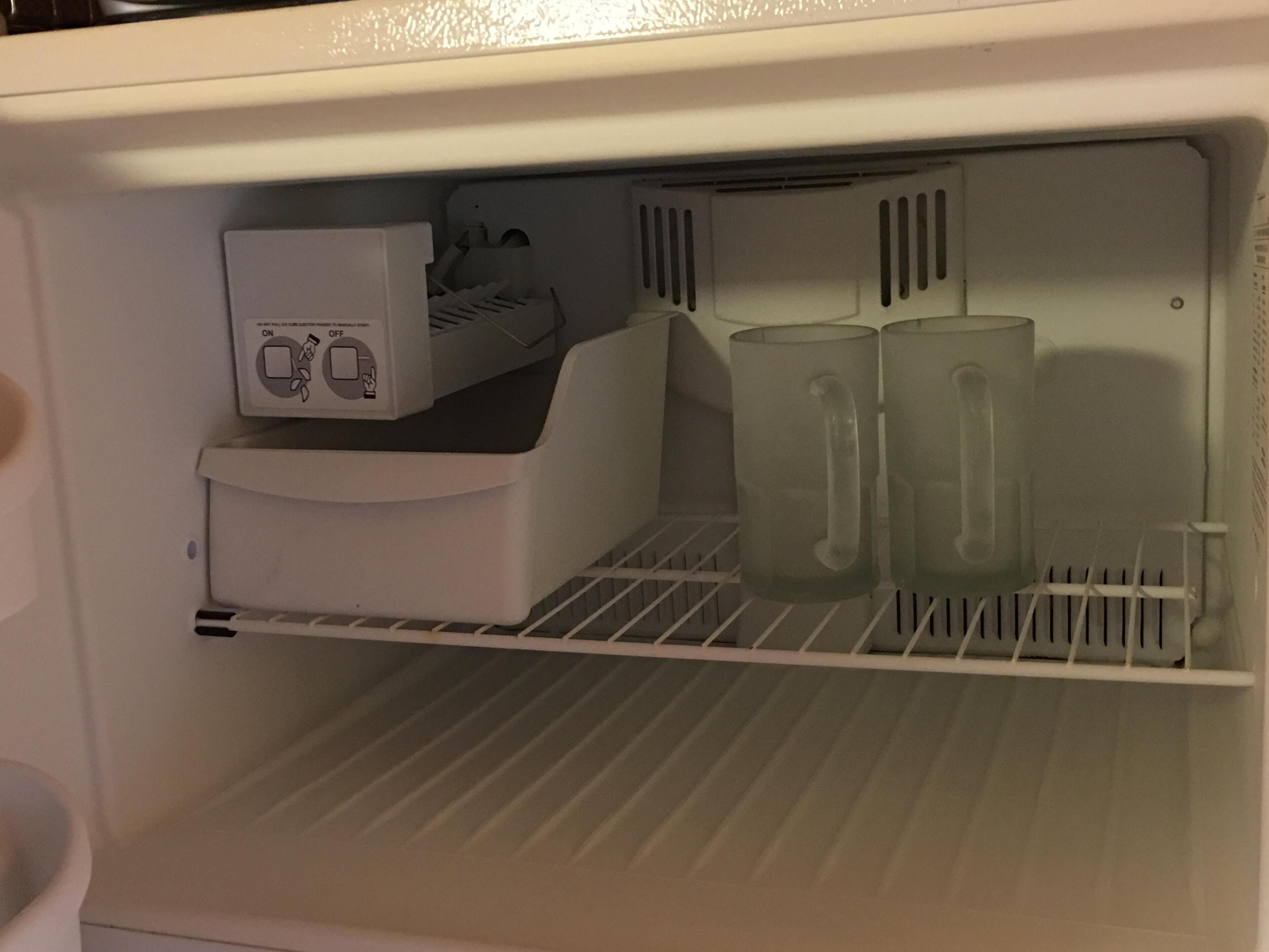 A refrigerator with a water dispenser and two glasses on the door shelf.