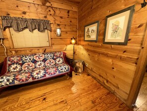 A cozy room with wooden walls, a quilted sofa, framed pictures, and a lamp.