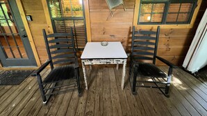 Une cabane en bois avec deux chaises noires, une petite table blanche et une porte dotée d’une fenêtre.