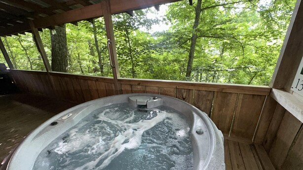 Un bain à remous avec une terrasse en bois et une vue sur une forêt.