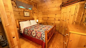 L’intérieur d’une cabane en bois, avec un lit, une petite table et un placard.