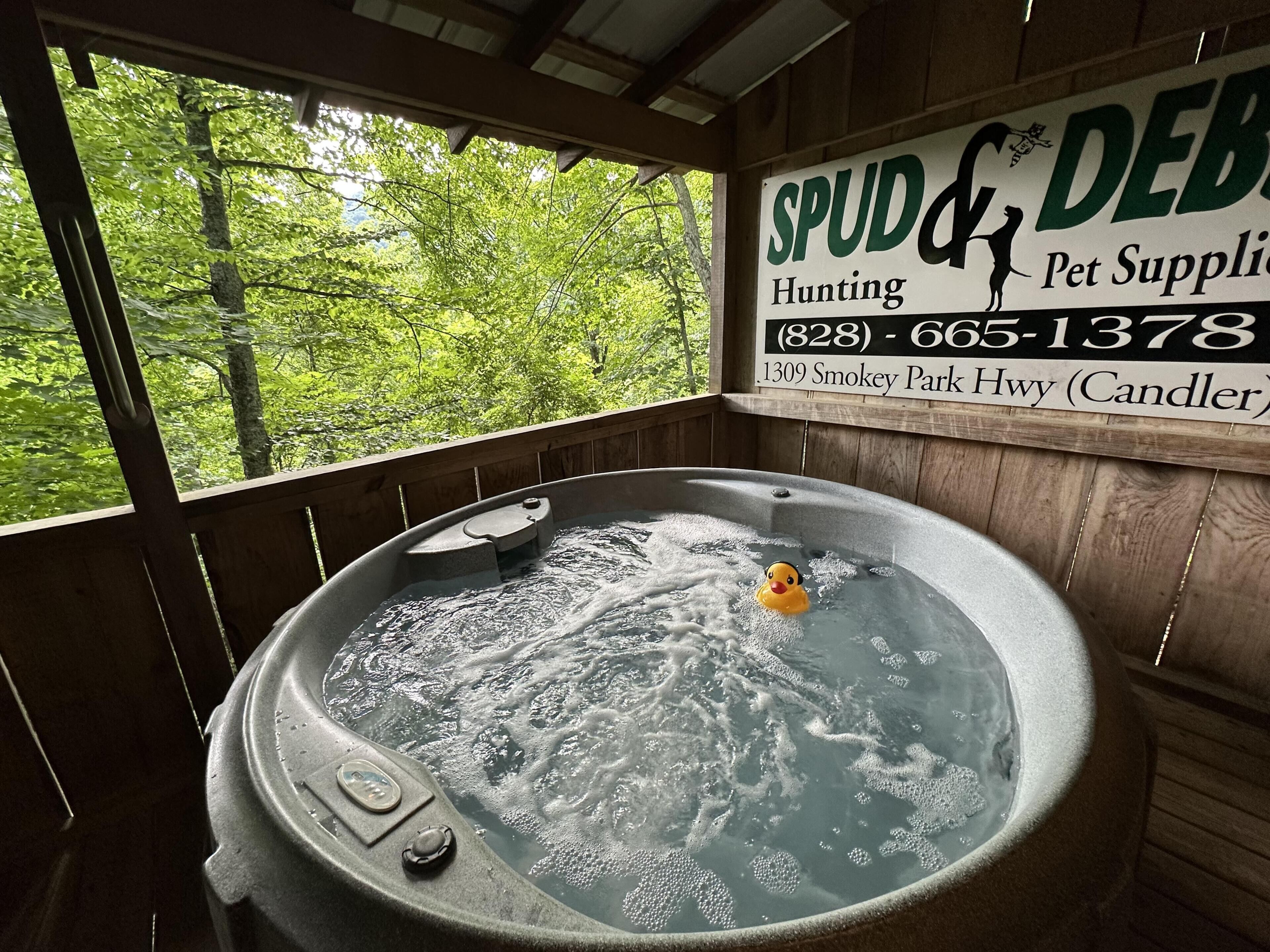 A hot tub with a duck, surrounded by wooden walls and a window with a forest view.