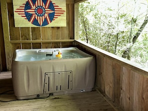 Een houten blokhut met een jacuzzi, een houten wand met een vlag en uitzicht op bomen.