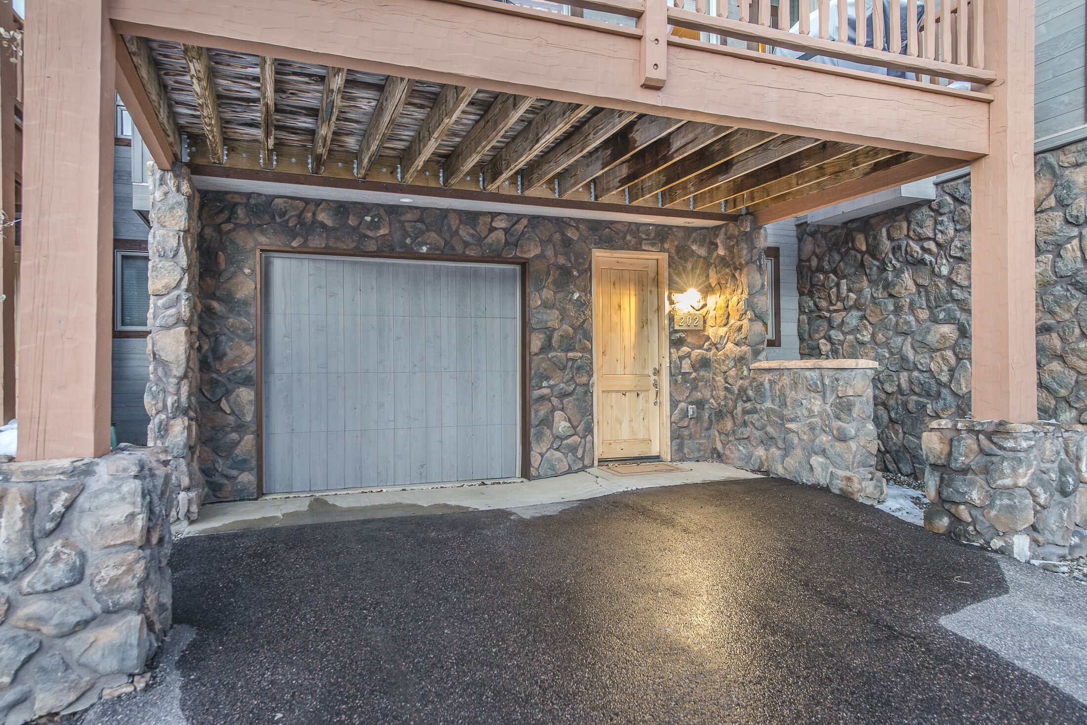 Eine Garage mit Überdachung, einer Steinwand, einer Holztür und einer Rollentür.