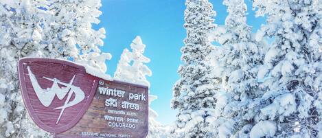 A sign for Winter Park Ski Area in Colorado, surrounded by snow-covered trees.