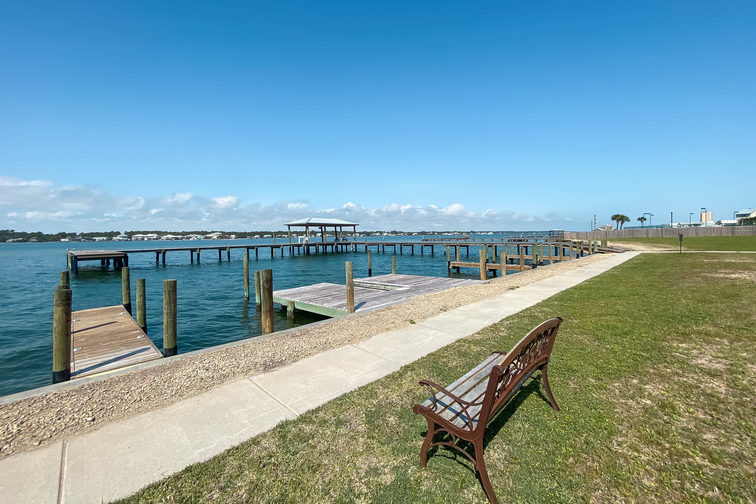 A waterfront park with a wooden pier, a bench, and a clear view of the water.