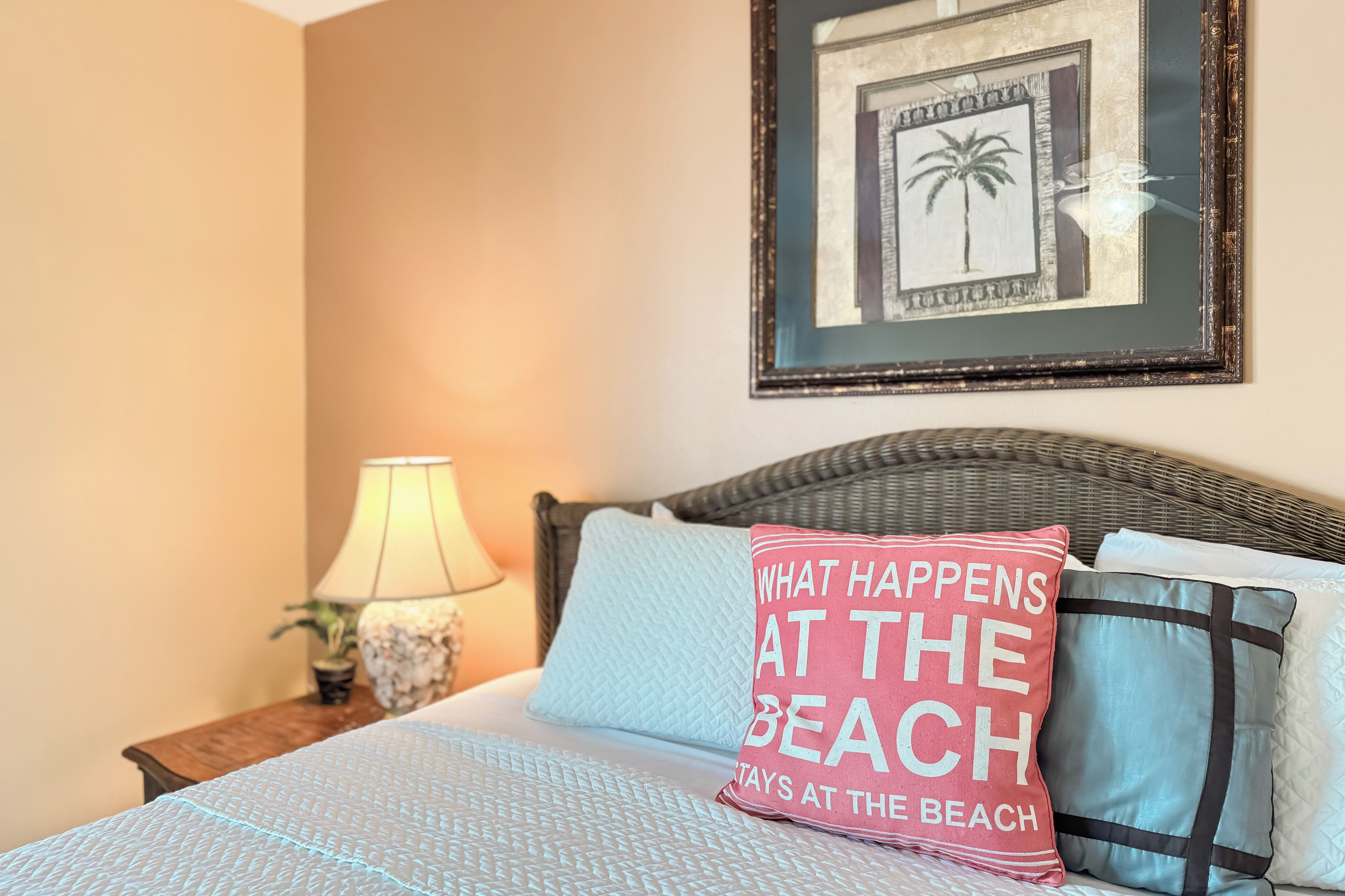 A neatly made bed with a patterned bedspread, a pillow with text, and a framed picture on the wall.