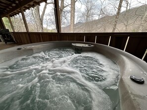 Ein Whirlpool mit einer Holterrasse und Blick auf Bäume und Hügel.