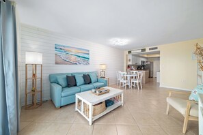 A living room with a blue sofa, a coffee table, a lamp, and a painting of a beach scene.