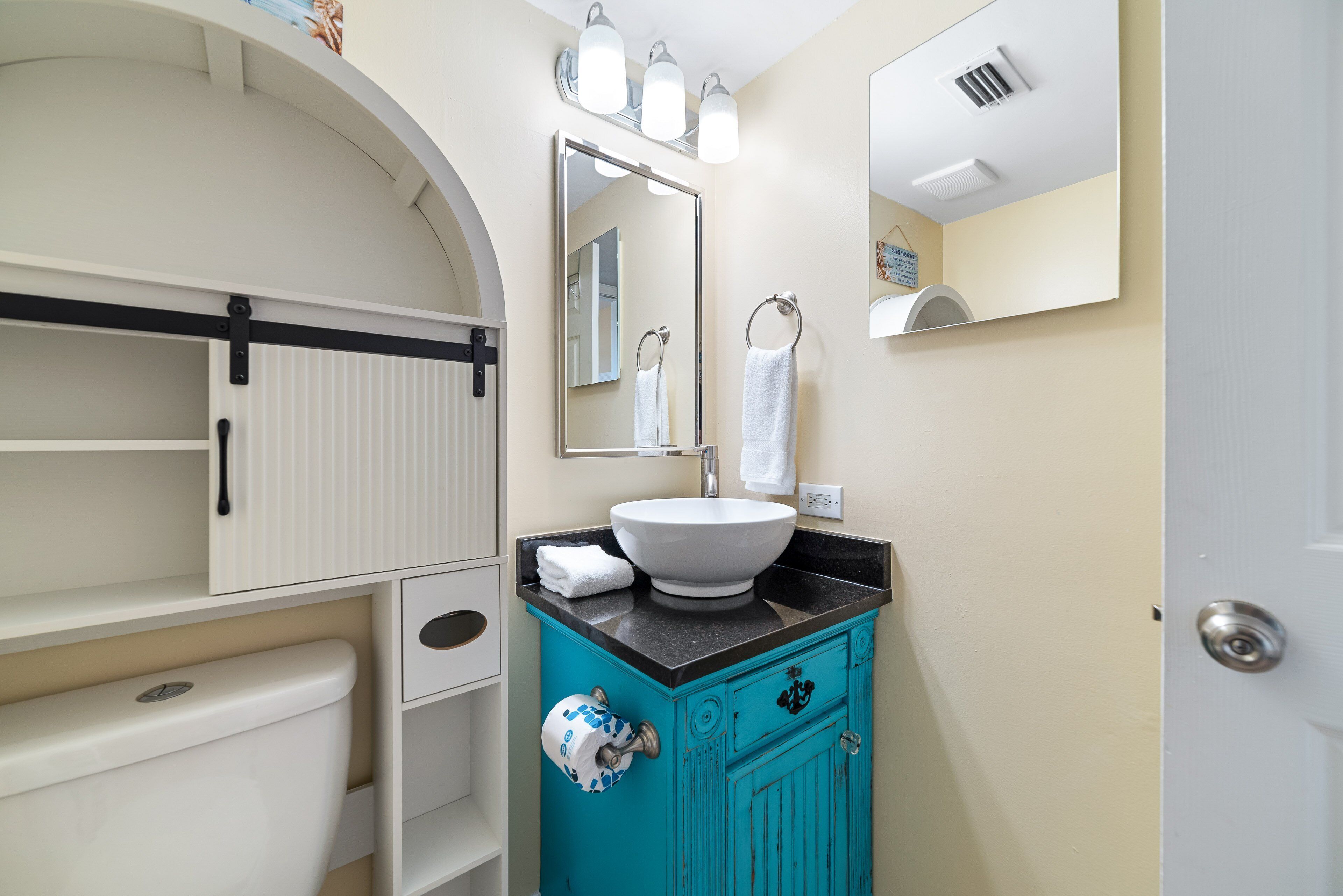 A bathroom with a white toilet, a turquoise sink vanity, and a large mirror above the sink.