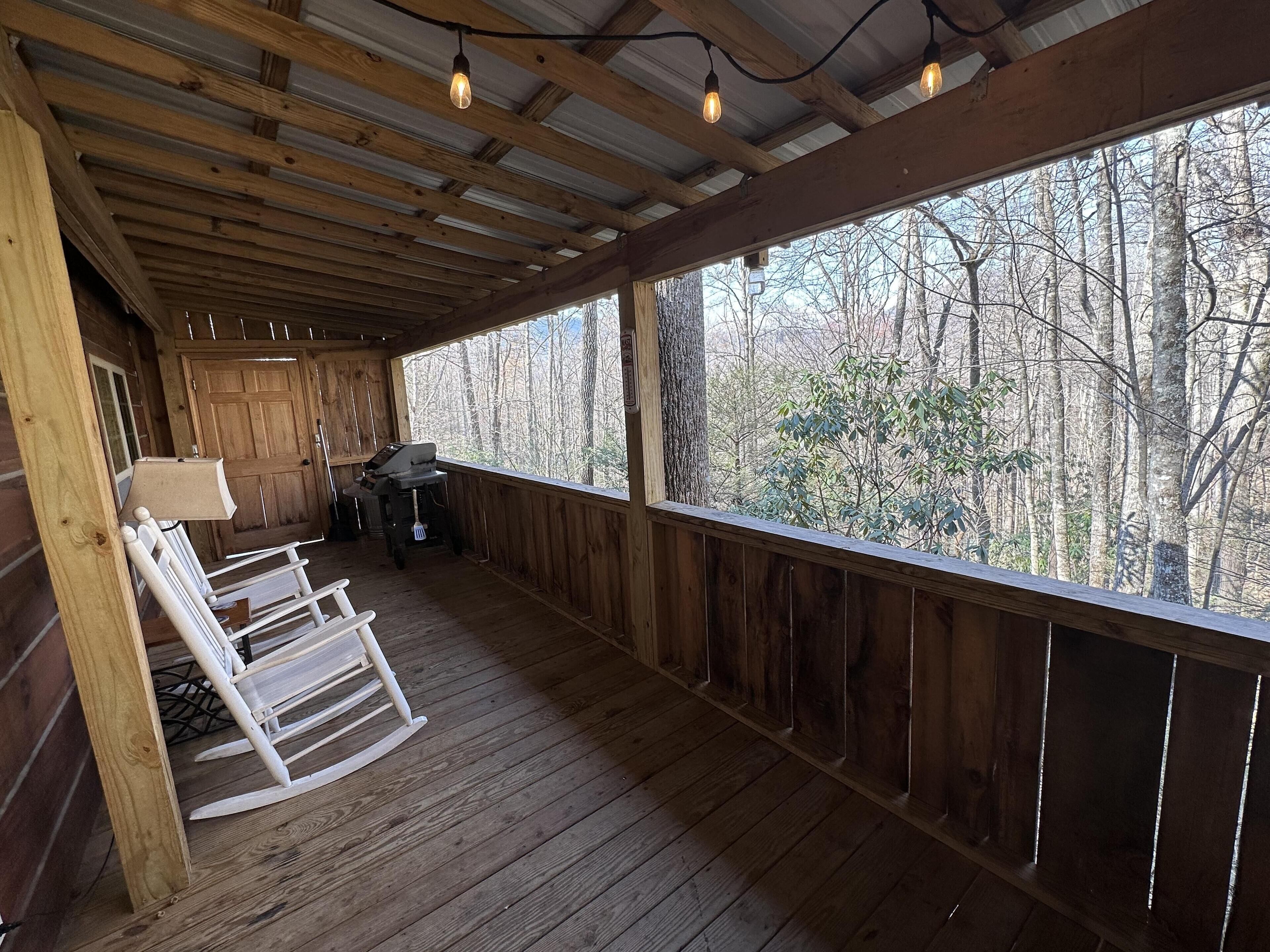 A wooden deck with rocking chairs, a grill, and a view of trees.
