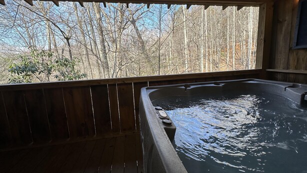 Een hottub met een houten terras en uitzicht op kale bomen.