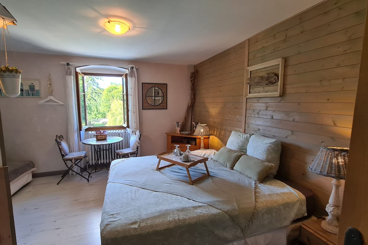 A cozy room with a bed, a small table with a lamp, a chair, and a window with curtains.
