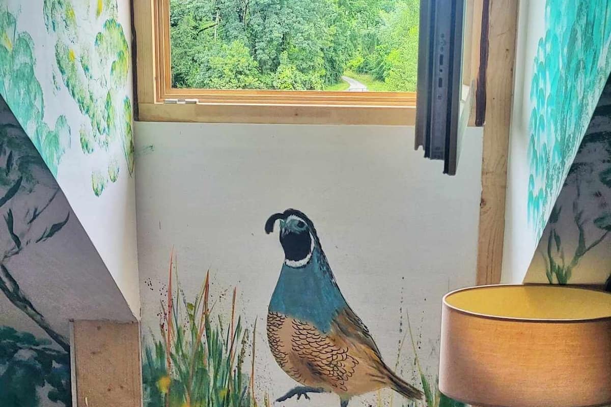 A room with a large window, a painting of a bird on the wall, and a lamp on the floor.