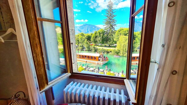 Aussicht aus dem Fenster auf einen Fluss mit Booten, umgeben von Grün und Bergen.