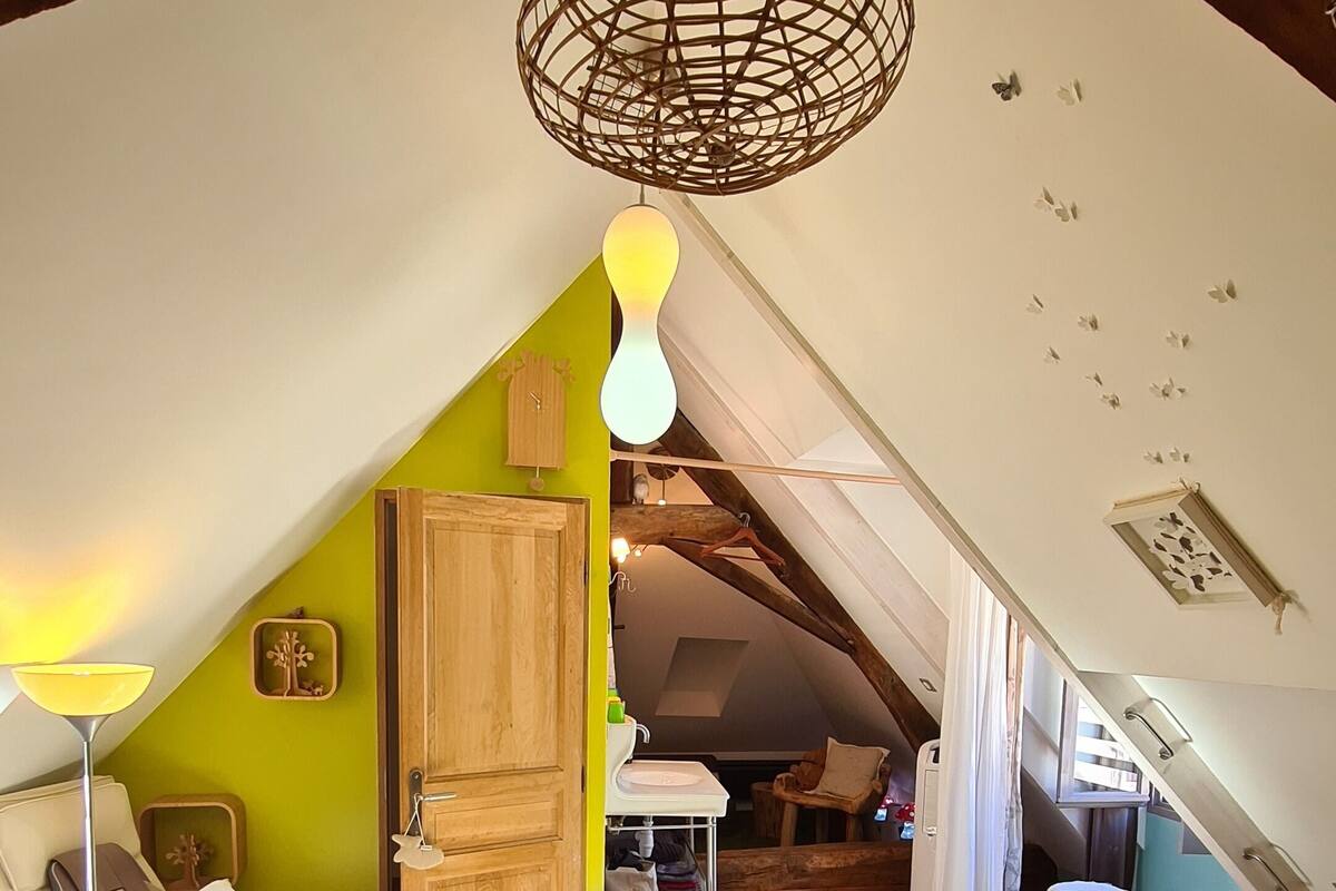 A cozy attic room with a dining table, chairs, a hanging light fixture, and a wooden door.