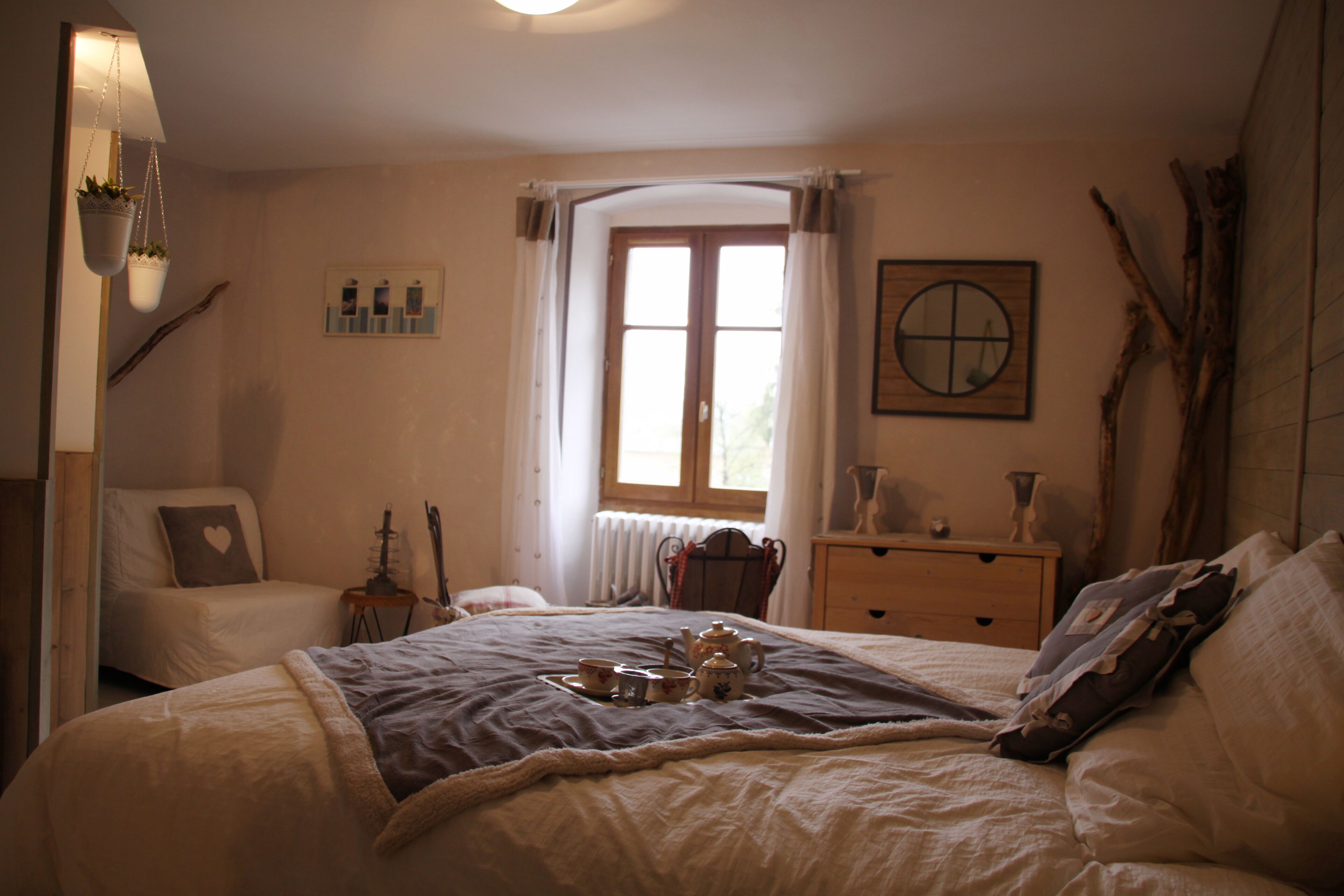 Un dormitorio con cama, una silla, un aparador, una ventana con cortinas y un cuadro colgado en la pared.