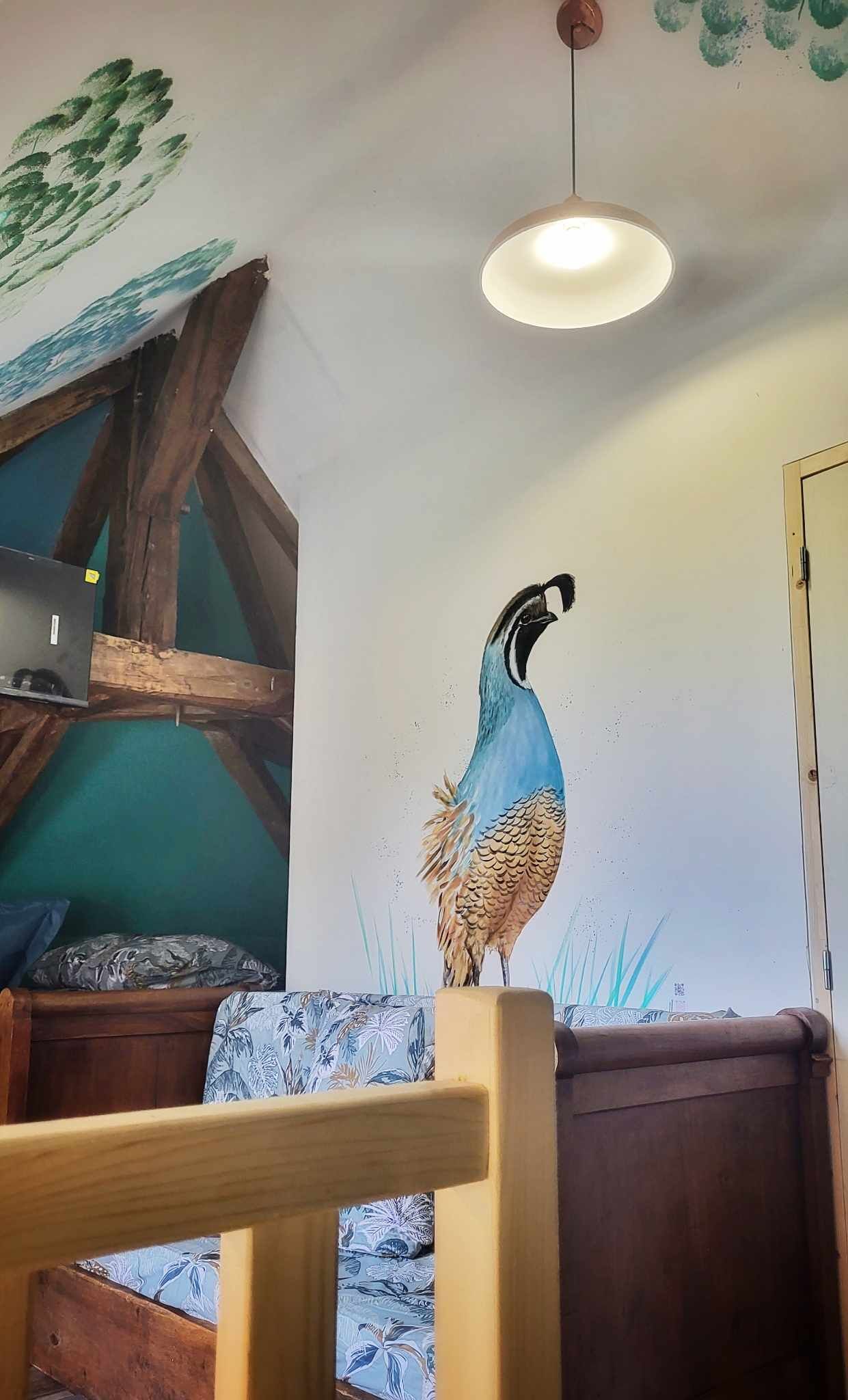 A room with a peacock mural, wooden furniture, and a ceiling light.