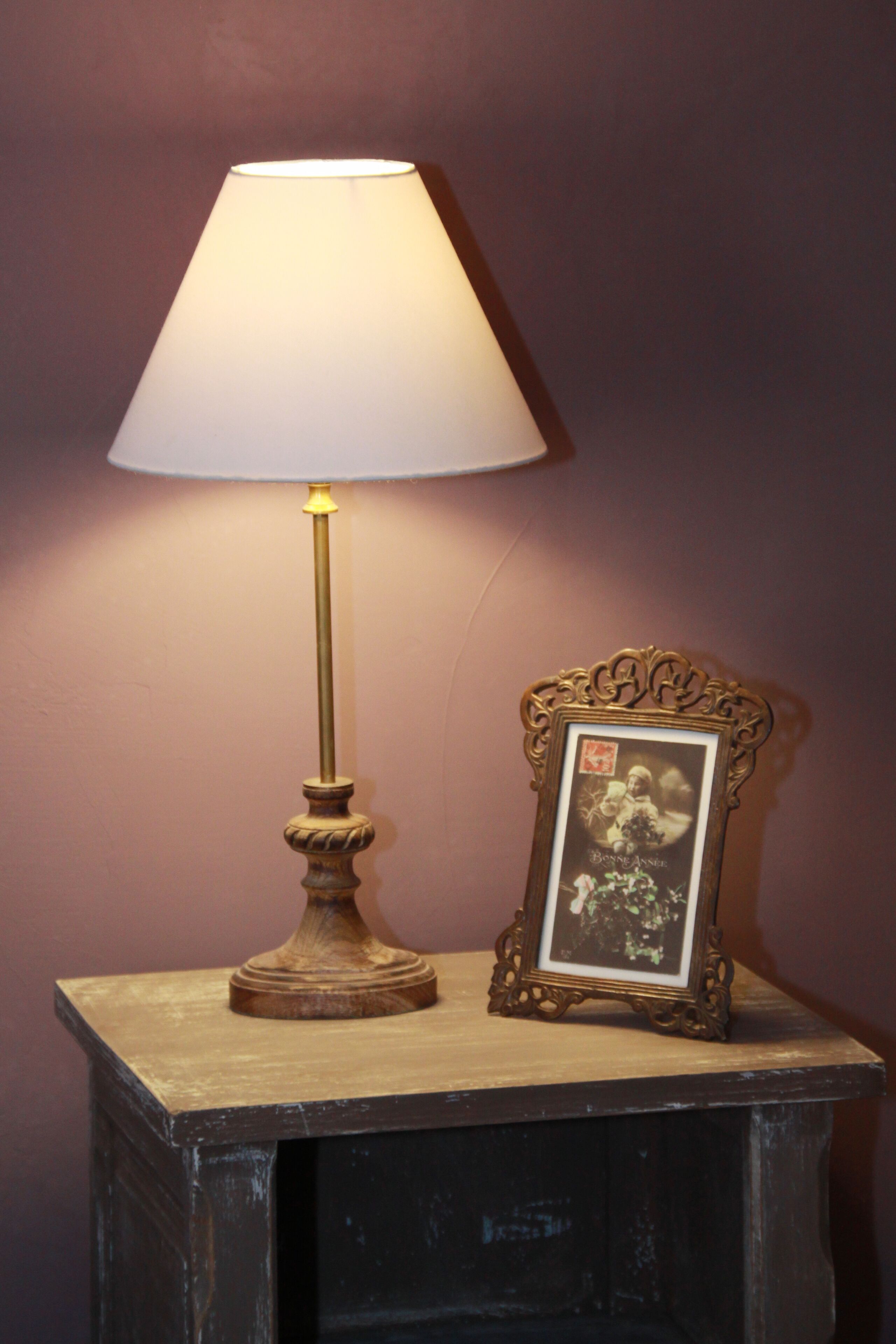 A table lamp with a white shade and a decorative frame with a picture on it.