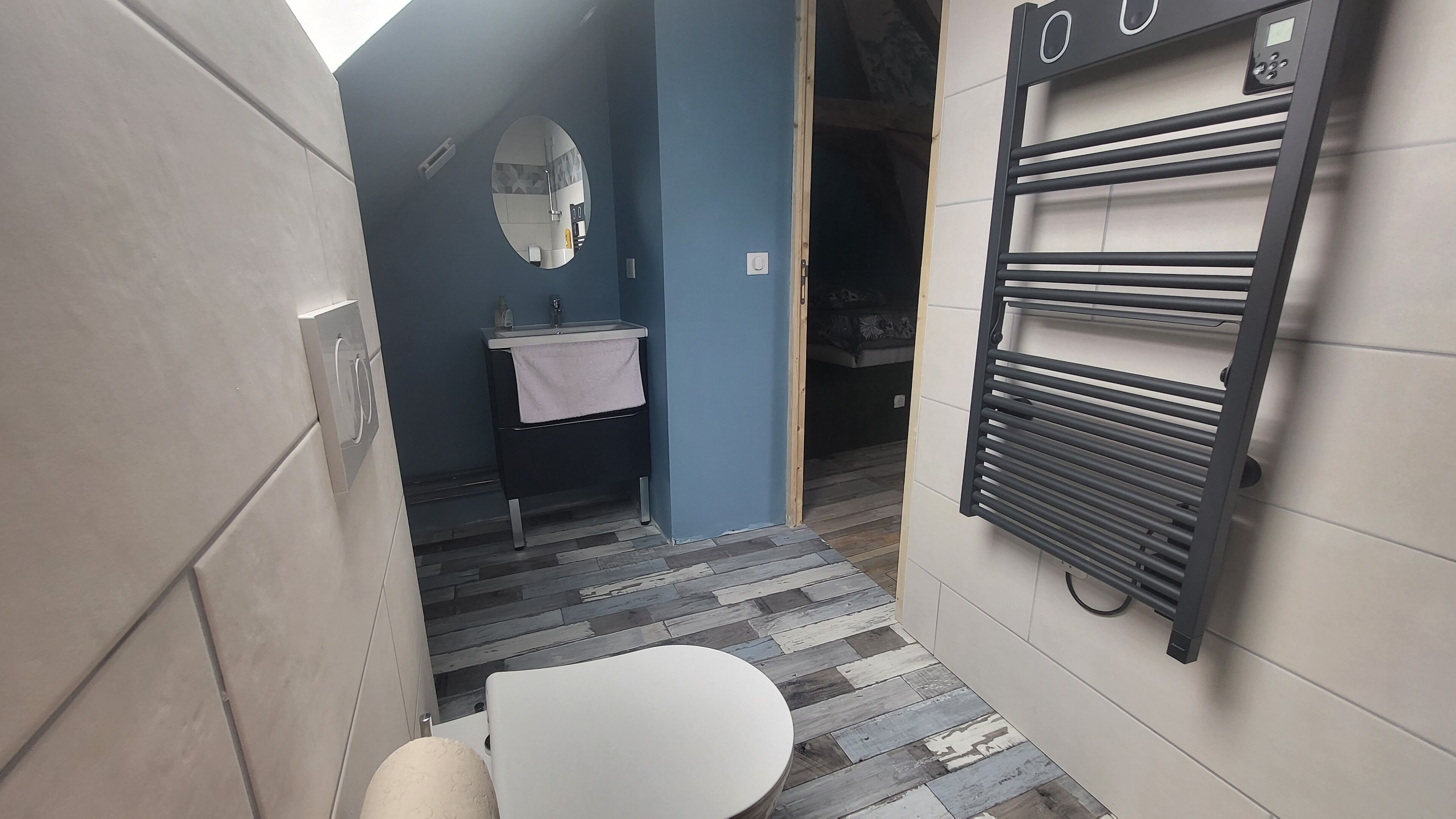 Une petite salle de bain avec des toilettes blanches, un lavabo avec une serviette, un miroir et un porte-serviettes.