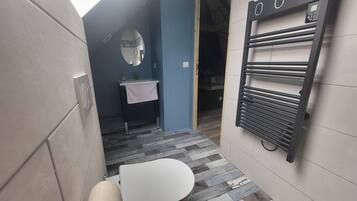 Une petite salle de bain avec des toilettes blanches, un lavabo avec une serviette, un miroir et un porte-serviettes.