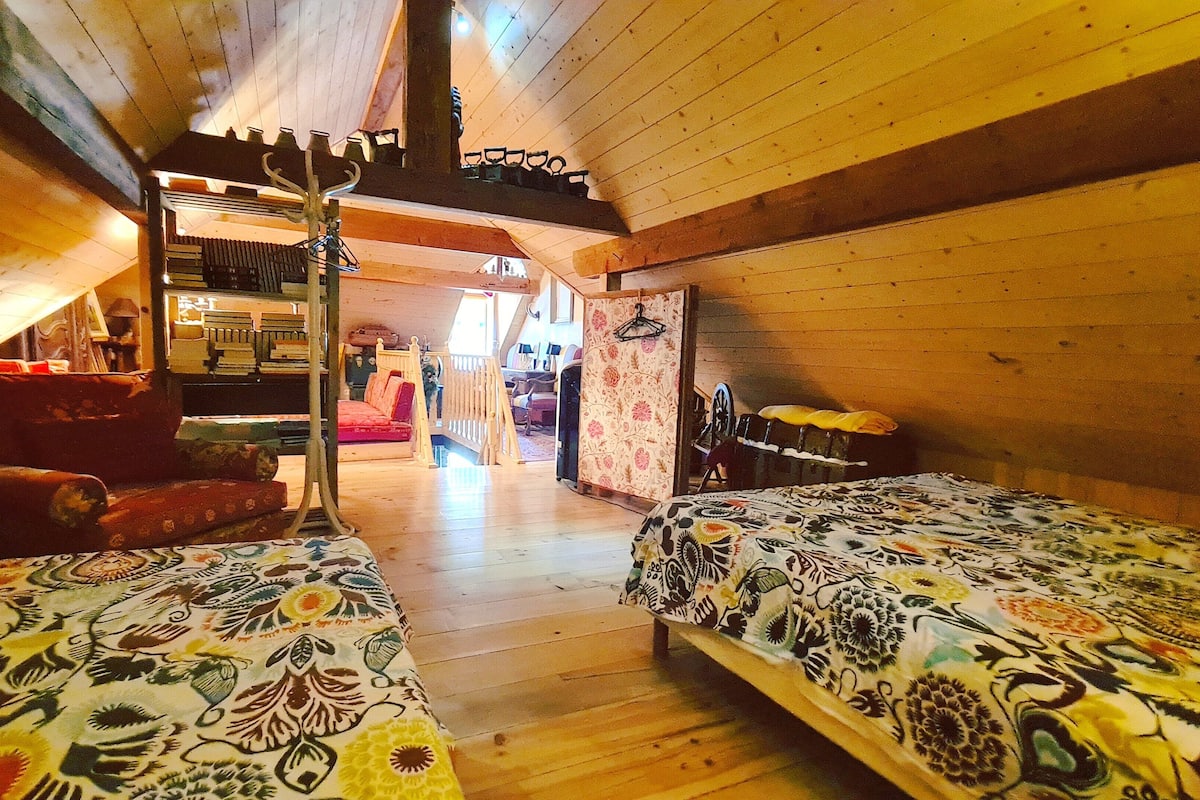 A cozy attic bedroom with two beds, a wooden ceiling, and a staircase leading to an upper level.