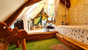 Ein gemütliches Schlafzimmer im Dachgeschoss mit schrägen Wänden, einem Boden aus grüner Kunstrasen, einer hölzernen Sitzbank und einem Badezimmer mit Steinwand und Dusche.