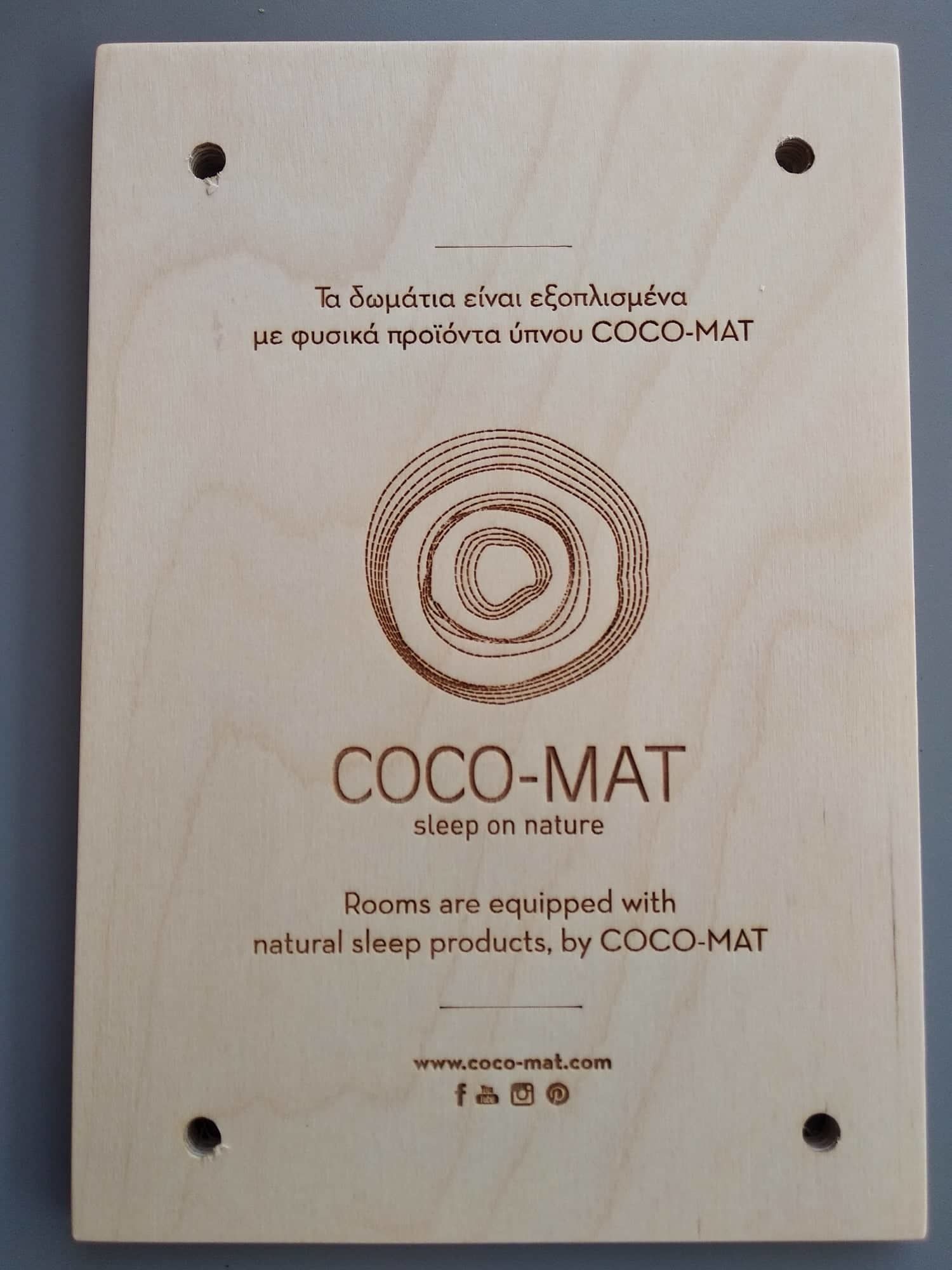 A wooden board with the text "COCO-MAT sleep on nature" and a website URL.