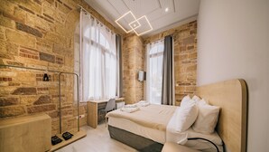 Un dormitorio moderno con una pared de piedra, un escritorio de madera, una cama con ropa blanca y una lámpara en el techo.