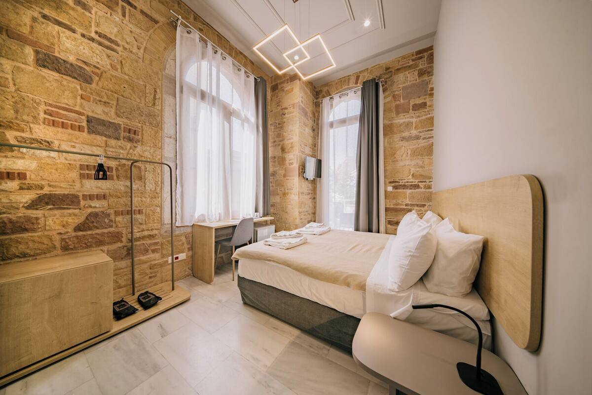 A modern bedroom with a stone wall, a wooden desk, a bed with white linens, and a ceiling light fixture.