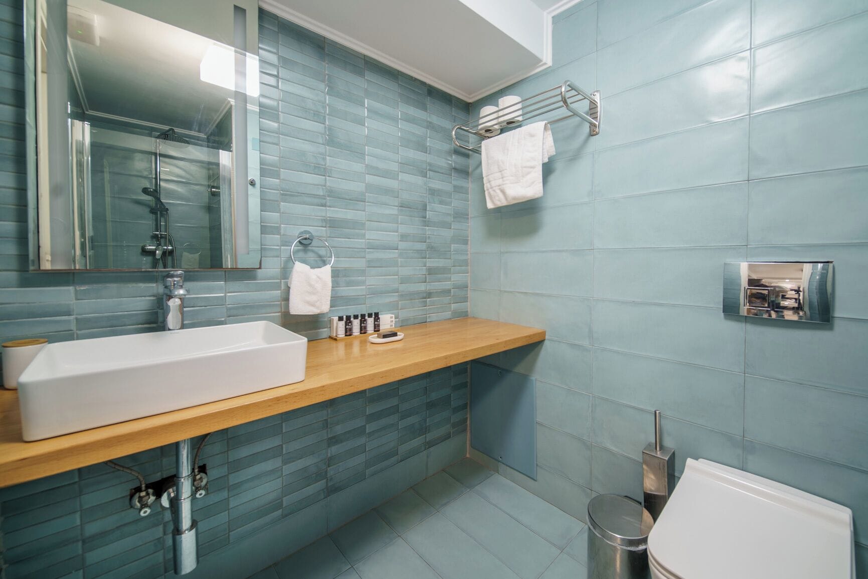 A modern bathroom with a rectangular sink, a mirror, a towel rack, and a toilet.