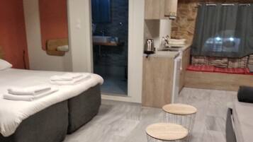 A modern hotel room with a bed, a small kitchenette, and a seating area with two stools.