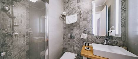 Une salle de bain moderne avec des carreaux à motifs, une douche en verre, un lavabo blanc et un plan de travail en bois.