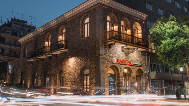 A stone building with arched windows and a balcony, labeled "MARKET IN" with a sign indicating it is a market.