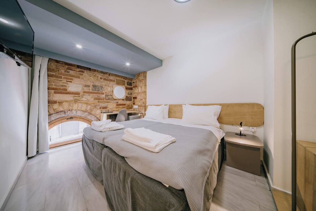 A modern bedroom with a stone wall, a bed with neatly folded towels, a bedside table, and a nightstand.
