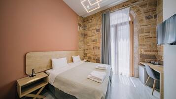 Una habitación de hotel moderna con pared de piedra, cama de madera, escritorio y televisor.