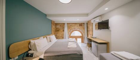 A modern hotel room with a large bed, a desk, a TV, and a stone wall.
