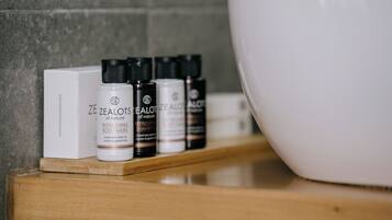Ein Badezimmerschrank mit Flaschen von ZEALOTS Duschgel und Shampoo sowie eine große weiße Waschtasche.