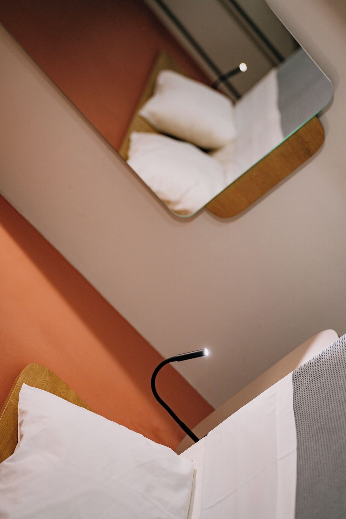 A hotel room with a bed, a bedside table, and a mirror reflecting a pillow and a wall.