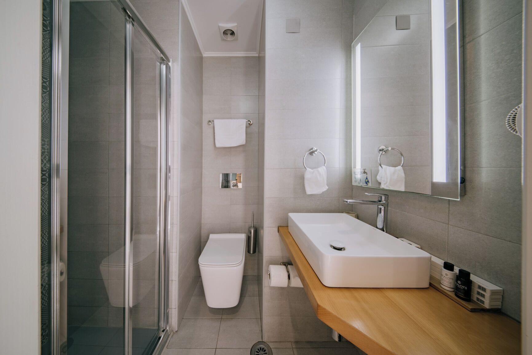 Un baño moderno con cabina de ducha de vidrio, un inodoro blanco, un lavabo con espejo y un mueble de tocador de madera.