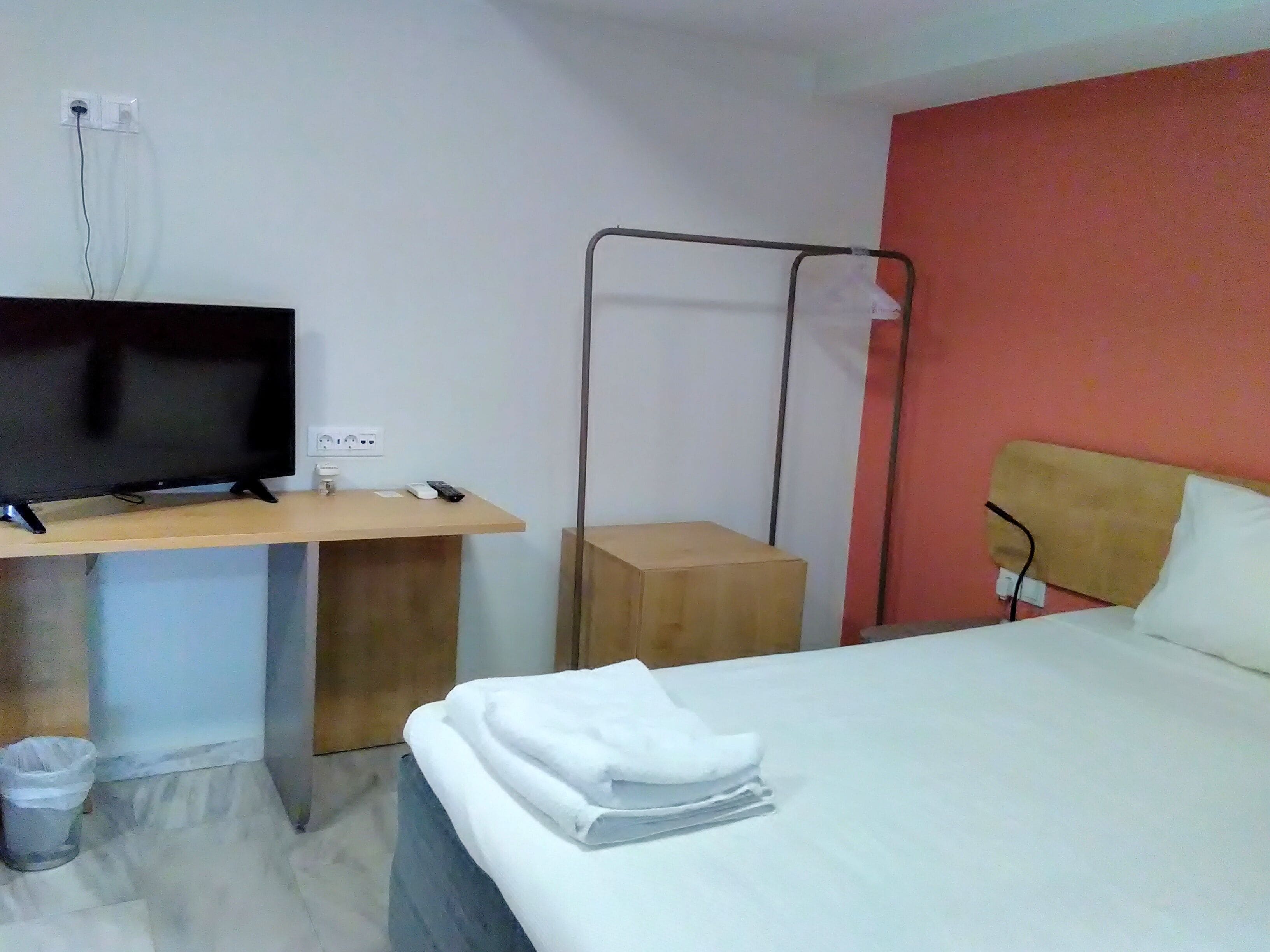 Une chambre d’hôtel comprenant un lit, un bureau avec une télévision, une prise électrique et une étagère fixée au mur.