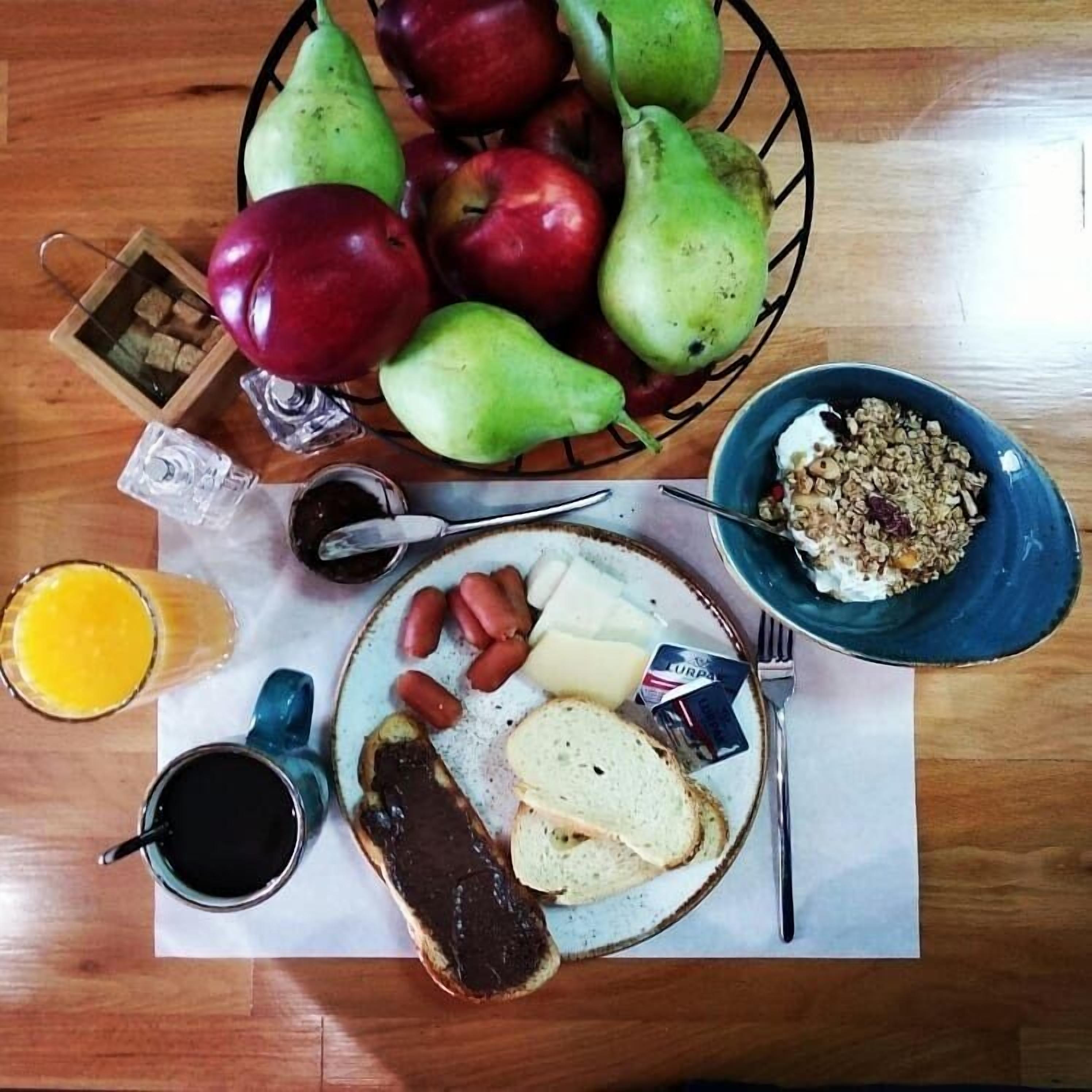 A breakfast table with a plate of food, a bowl of cereal, a glass of orange juice, and a basket of fruit.