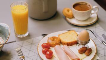 A breakfast setting with a plate of eggs, ham, cheese, tomatoes, and bread, a glass of orange juice, a cup of coffee, and a small plant on a table.