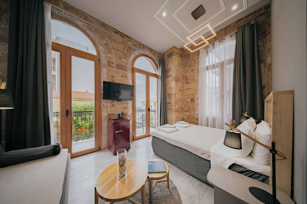 A modern hotel room with a large bed, a small desk, a TV, and a balcony with a view.