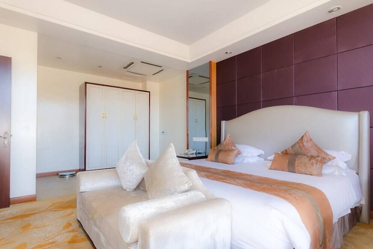 A hotel room with a large bed, a sofa, a wardrobe, and a mirror.