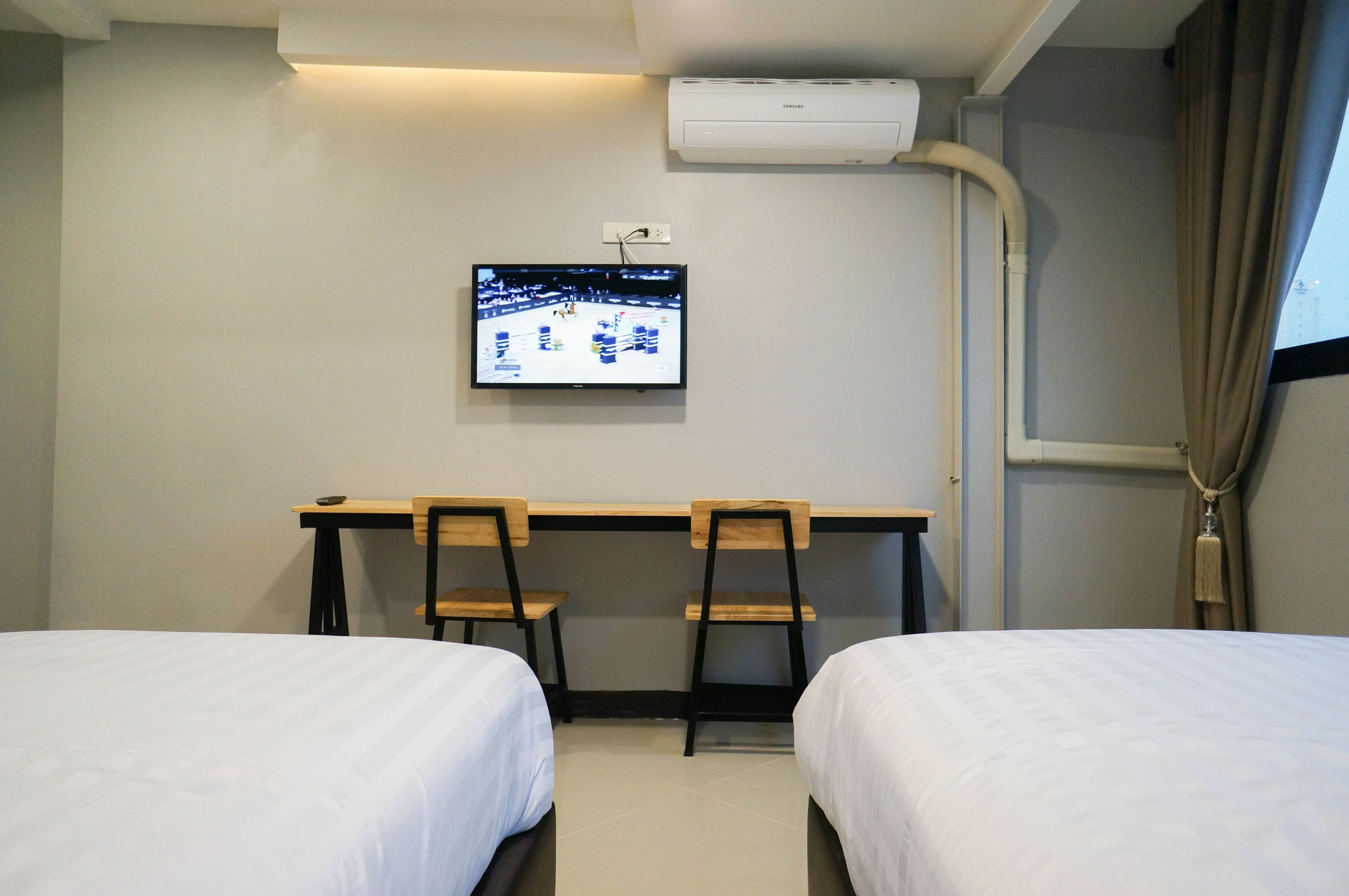 Une chambre d’hôtel avec deux lits, un bureau avec des chaises, un téléviseur fixé au mur et un appareil de climatisation.