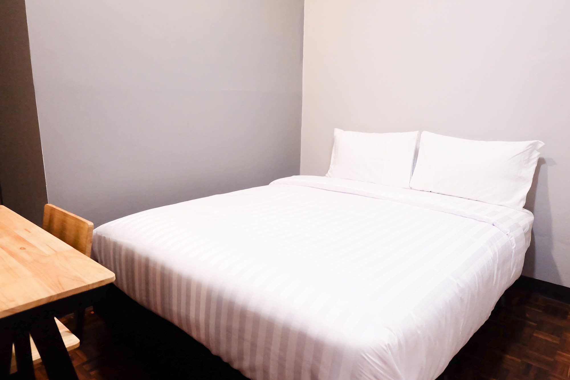 A neatly made bed with white bedding in a room with a wooden table and chairs.