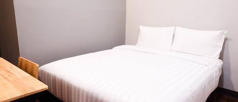 A neatly made bed with white bedding in a room with a wooden table and chairs.