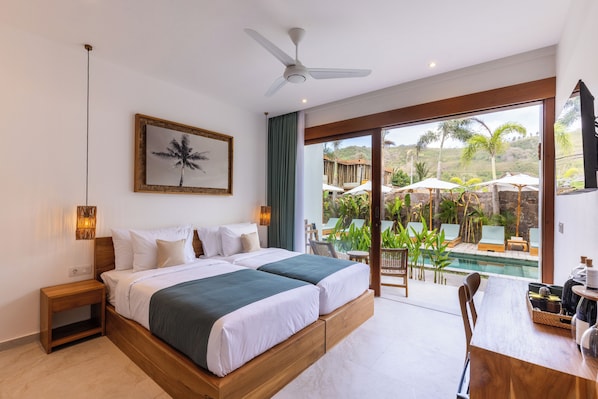 A bedroom with a large bed, a ceiling fan, a framed picture, a nightstand, and a view of an outdoor pool area. - Sikara Lombok Hotel (Kuta)